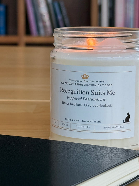 Close view of the Recognition Suits Me candle label with the Peppered Passionfruit scent line, books behind