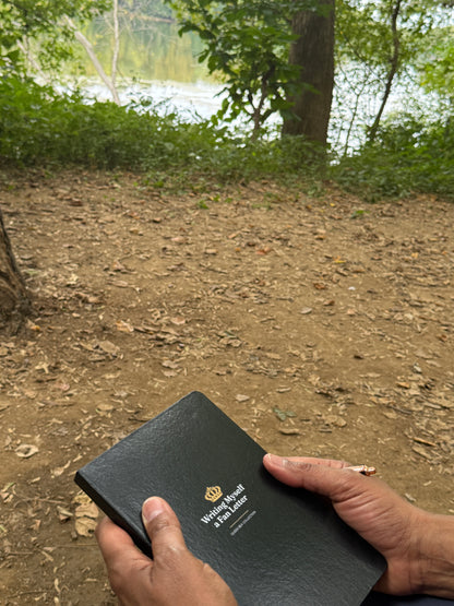 The black Writing Myself a Fan Letter journal held outdoors, lake behind