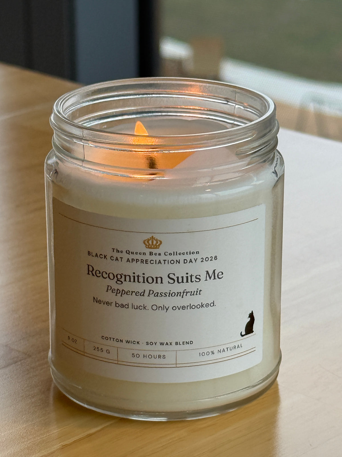 Recognition Suits Me candle against a dark wall, the white label in sharp contrast
