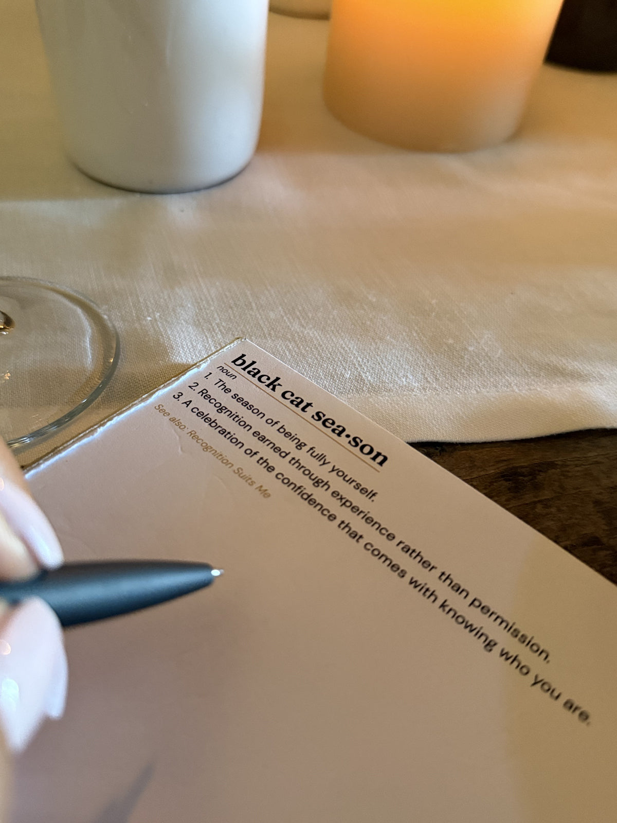 A hand writing on the Black Cat Season notepad at a candlelit table