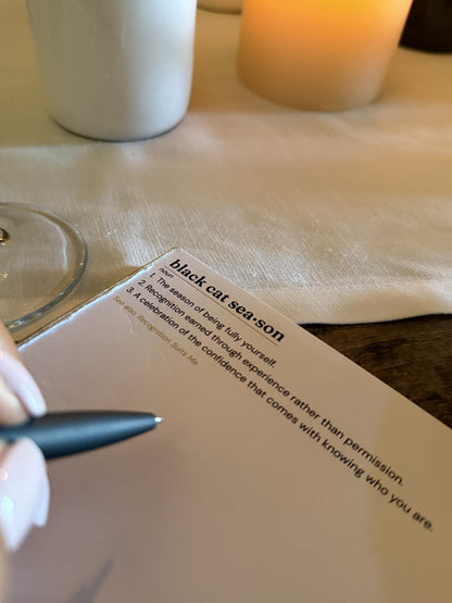 A hand writing on the Black Cat Season notepad at a candlelit table