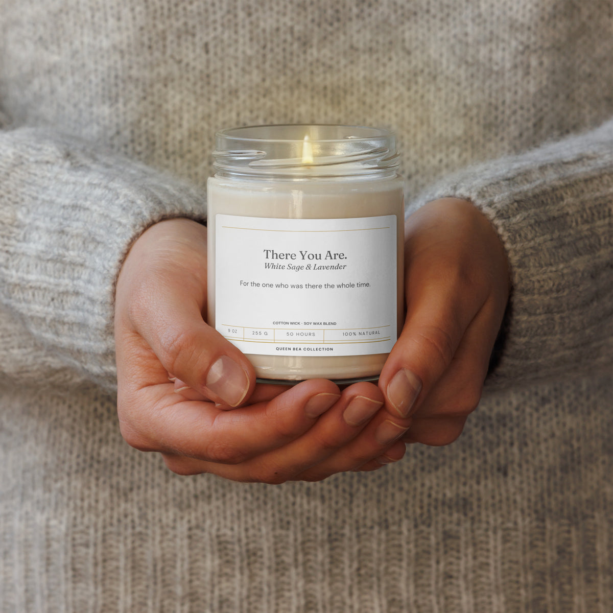 Two hands cradling the There You Are candle, lid on, grey knit sleeves